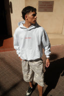 Person wearing a light gray hoodie with red text and camouflage shorts standing on a patterned floor.